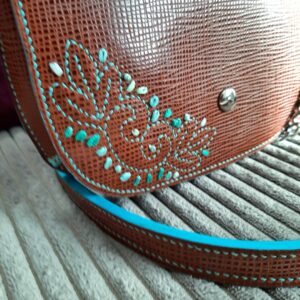 Détail de la broderie sur le rabat. Broderie dans les camaïeux de bleus turquoises