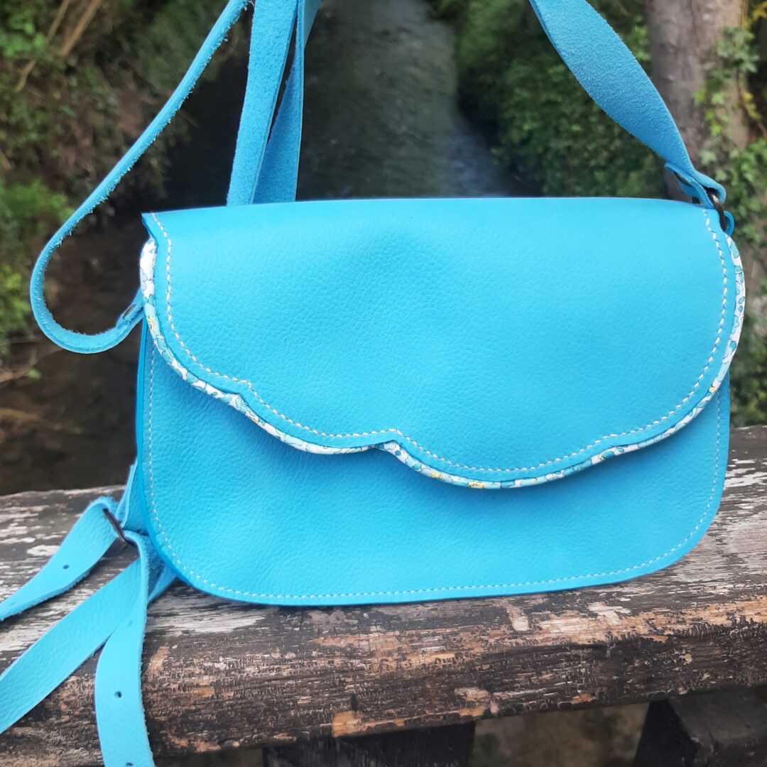 Petit sac bandoulière artisanal en cuir turquoise, bordé d’un biais Liberty, doublé en cuir d’agneau bleu pâle, avec bandoulière réglable.