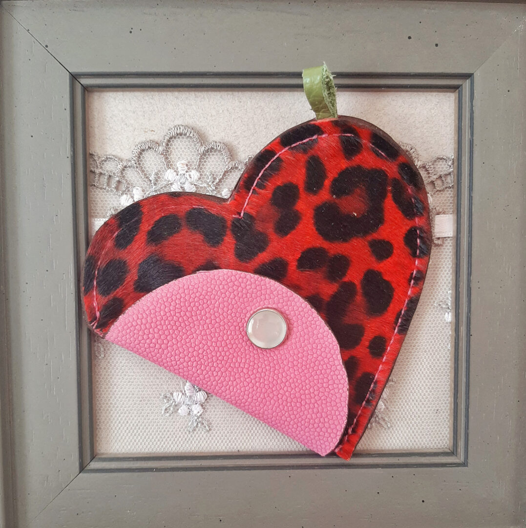 porte-monnaie coeur est réalisé avec un cuir poilu, imprimé de motifs imitation panthère rouge. son rabat est en cuir fluo rose, et se ferme par un bouton pression nacré.