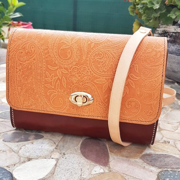 Sac porté épaule ou en bandoulière croisé sur le devant. Rabat en cuir naturel tannage végétal de couleur naturelle, avec motif embossé style cachemire. Fermeture par un touret métallique doré. Corps du sac en cuir tannage vegétal de couleur marron chocolat. Cousu à la main au point sellier avec du fil de lin assorti.