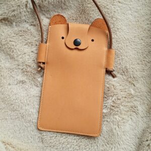 Cuir tannage végétal orange, légèrement velours. Son nez qui sert de rabat, se ferme par un bouton pression de couleur noir. Se porte en bandoulière ou porté épaule, par une bandoulière amovible en lanière de cuir rond, qui se règle en faisant un nœud.