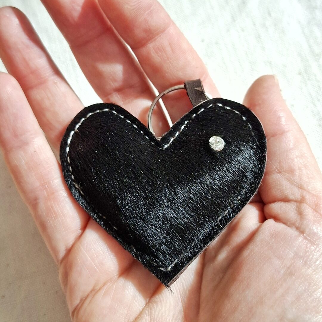 Porte-clés forme de coeur en cuir poilu de vache de couleur noir. Il est présenté dans une main. Mousqueton argenté