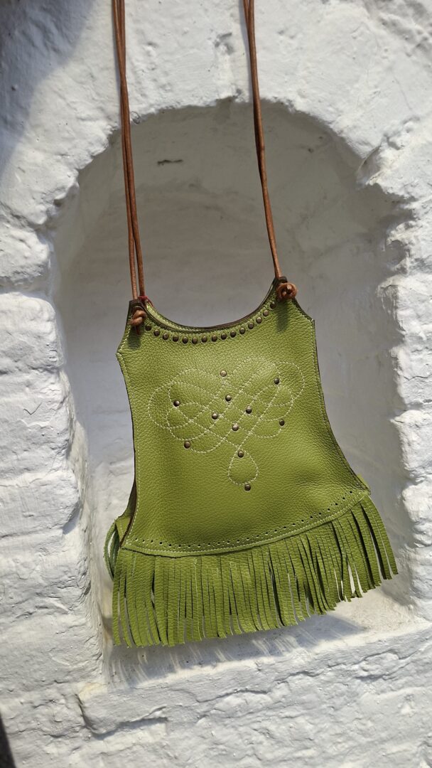 Sac en cuir pleine fleur couleur vert pistache. Franges coupées à la main au bas du sac. Rivets en laiton vieilli sur le bord haut du sac, qui sont alignés. Motif arabesque sur la face cousu à la main au point sellier. Forme originale bandoulières lanières ronds en cuir naturel. Elles peuvent être réglables grâce à ses nœuds.