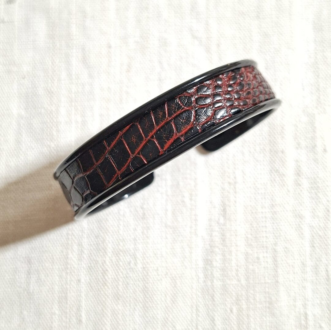 bracelet manchette en métal noir et cuir d'alligator noir avec dans les creux une teinte de rouge. Le bracelet est réglable à votre poignet. Pièce unique