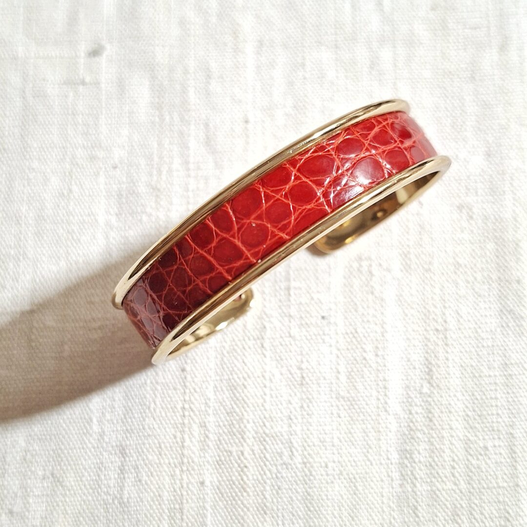 bracelet manchette en métal doré et cuir d'alligator rouge vernis brillant. Le bracelet est réglable à votre poignet