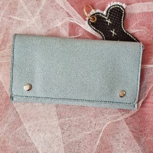 Compagnon en Epsom de couleur bleu gris. Deux boutons pressions métalliques argenté sur le rabat permettent de bien fermer cette pochette compagnon. Couture main au point sellier au fil de lin couleur bleu.