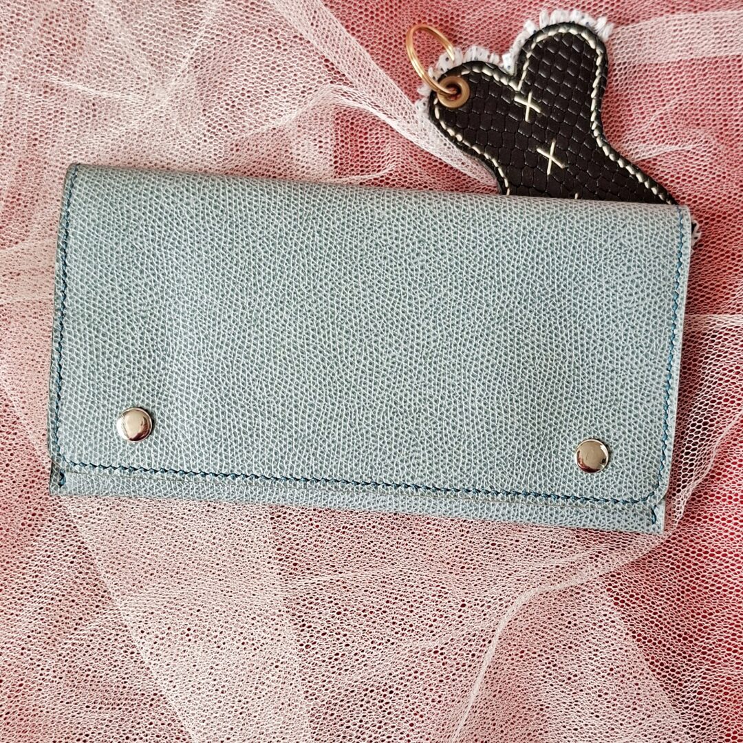 Compagnon en Epsom de couleur bleu gris. Deux boutons pressions métalliques argenté sur le rabat permettent de bien fermer cette pochette compagnon. Couture main au point sellier au fil de lin couleur bleu.