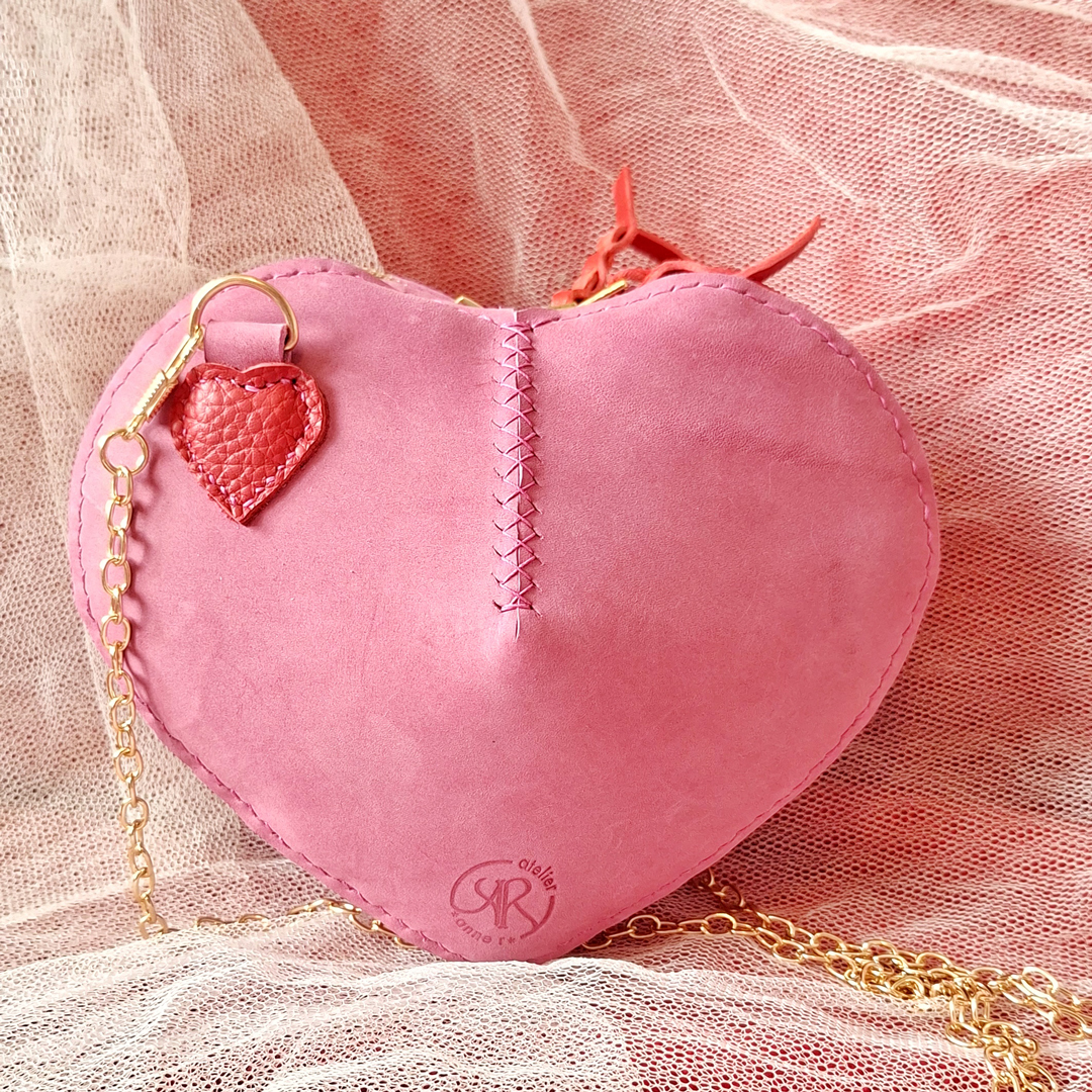 sac en cuir tannage végétal rose toucher velours en forme de coeur. Cousu main au point sellier avec un fil de lin. Fermeture à glissière doré avec double curseur. Bandoulière chainette doré amovible.