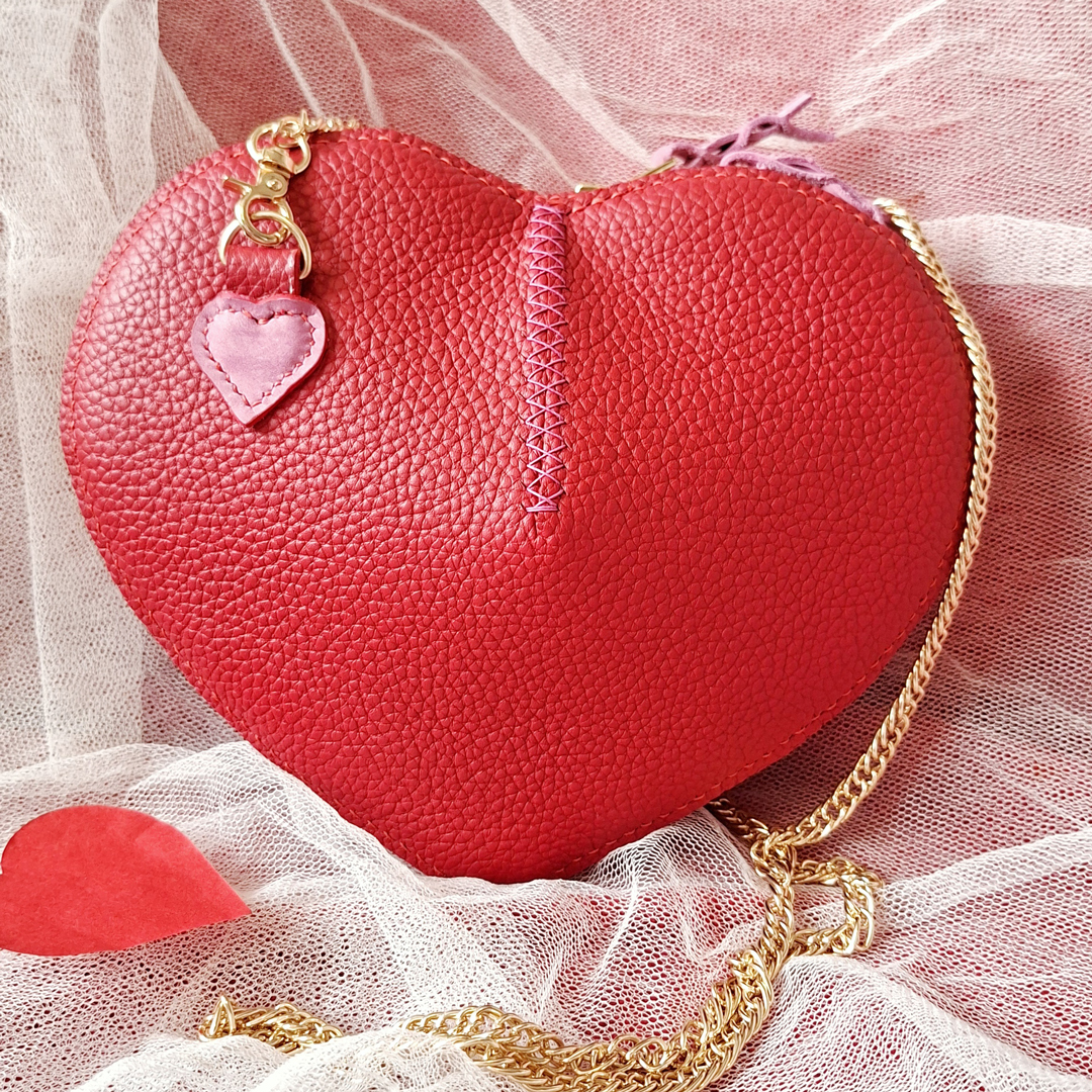 Sac en cuir pleine fleur grainé rouge en forme de coeur. Cousu main au point sellier avec du fil de lin rouge. Fermture à glissière doré avec double curseur. Bandoulière chainette doré amovible.
