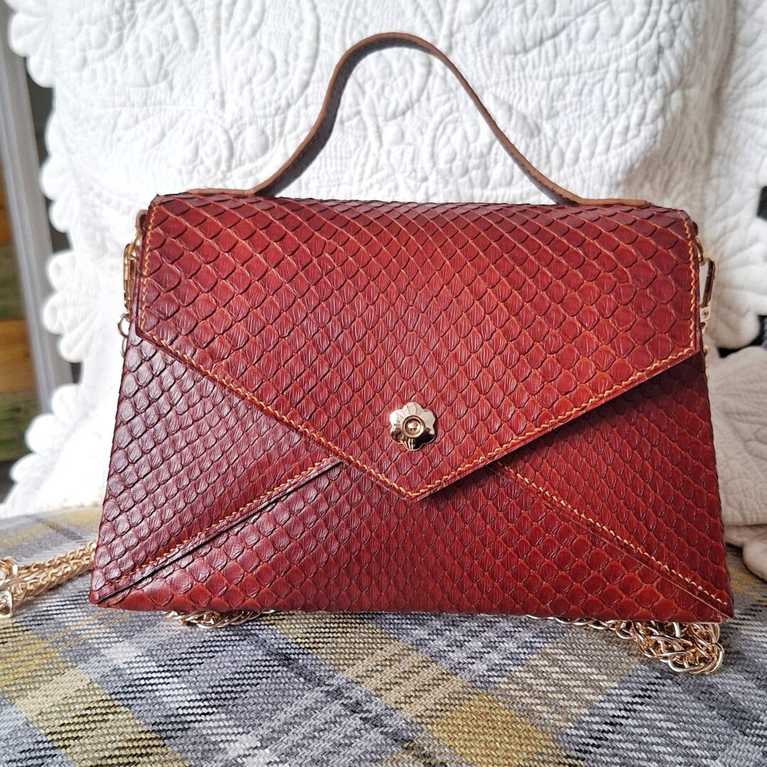Vue de face du sac à main en cuir de python acajou avec rabat enveloppe, poignée et fermeture fleur dorée.