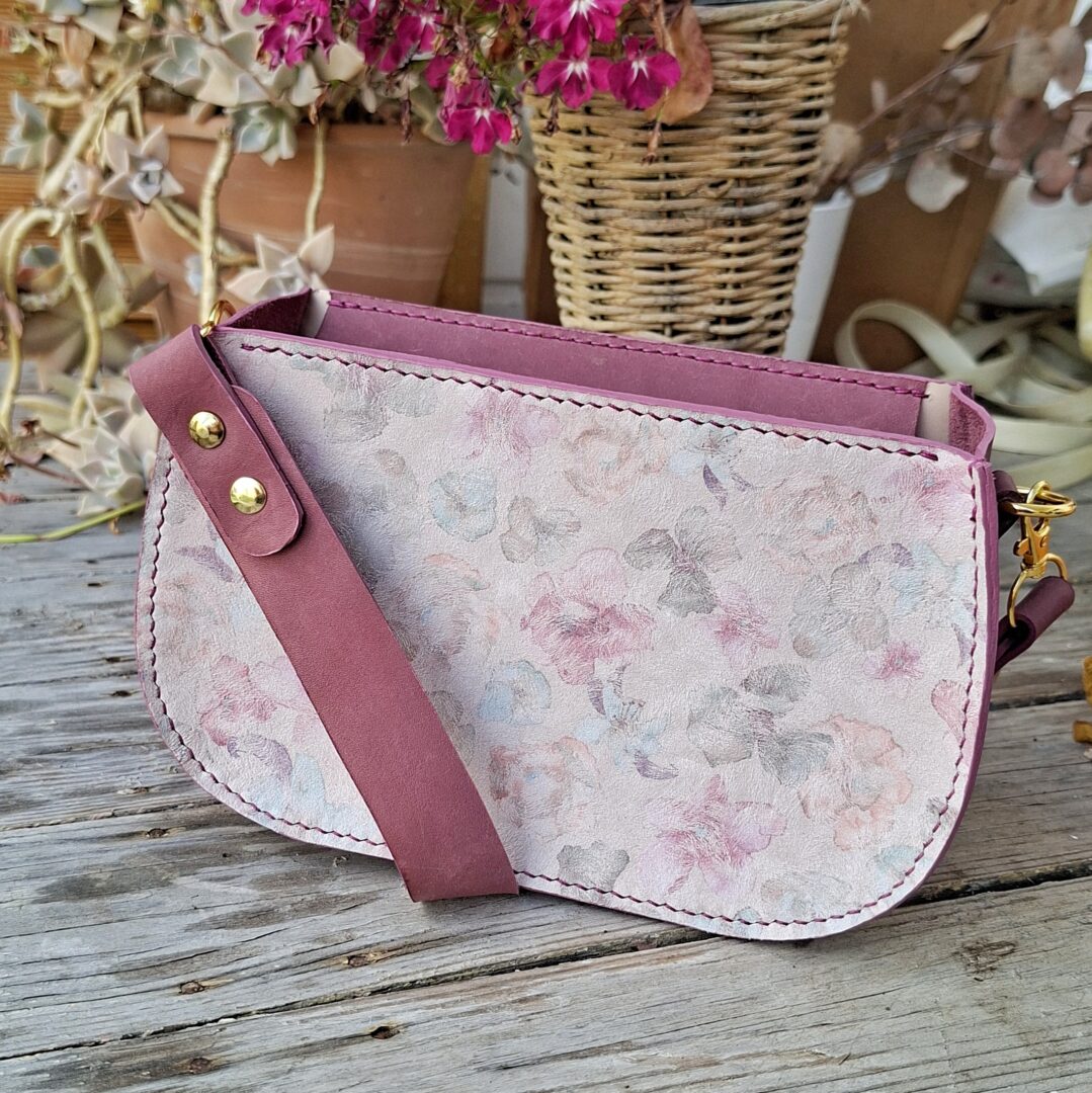 Sac artisanal en cuir fleuri et cuir pleine fleur lie de vin posé sur une table en bois.