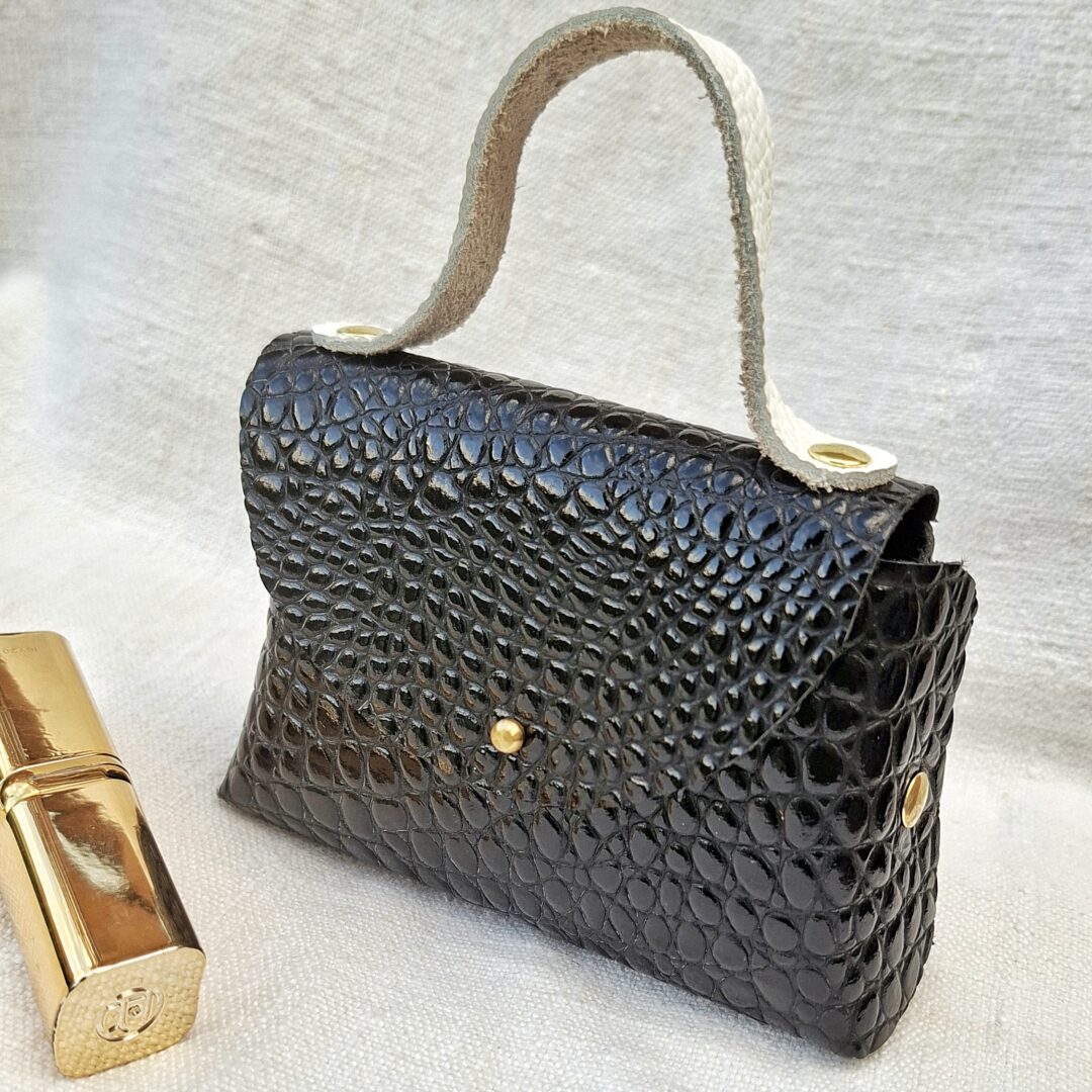 Petit sac en cuir de chèvre verni noir imitation crocodile, fabriqué à la main avec poignée en cuir pleine fleur blanc cassé et fermeture par bouton de col.