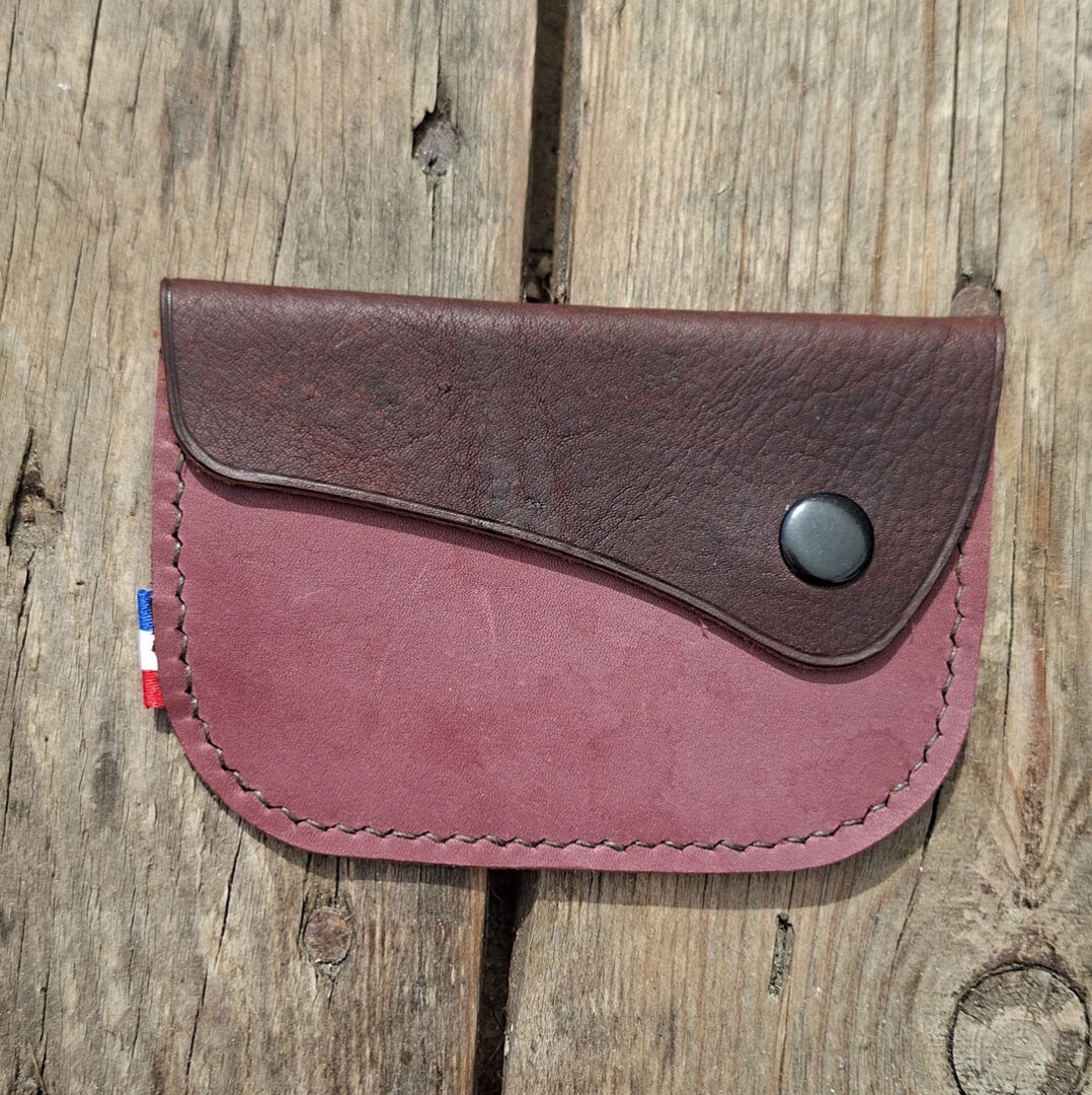 Porte-monnaie artisanal en cuir pleine fleur violet à tannage végétal légèrement suédé, avec rabat en cuir brun et fermeture par bouton pression raisin.
