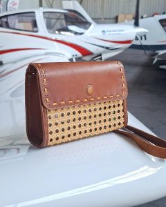 Sac cartouchière en cuir cognac et osier tressé photographié sur un avion, création artisanale française