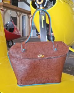Vue de face d'un sac à main en cuir pleine fleur marron chocolat, bordures turquoise et fermeture à tourniquet dorée.