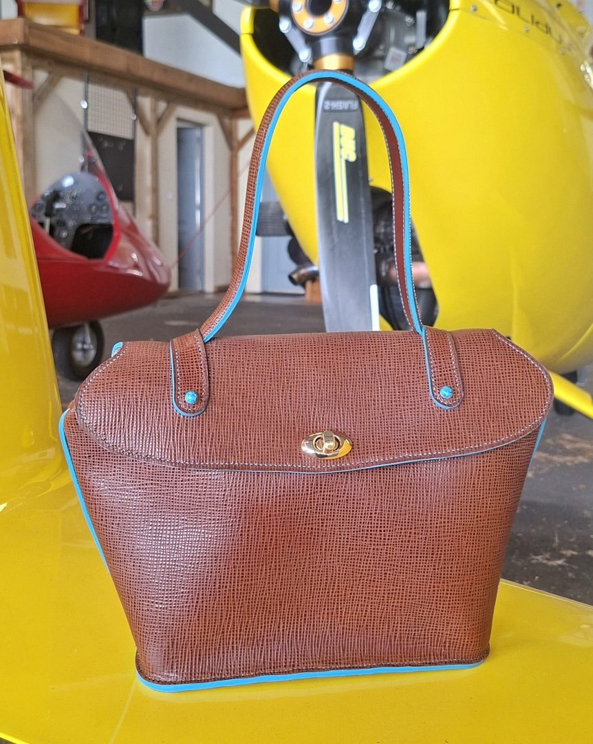 Vue de face d'un sac à main en cuir pleine fleur marron chocolat, bordures turquoise et fermeture à tourniquet dorée.